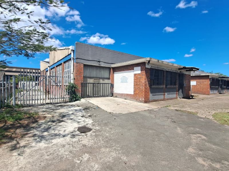 Front view of an industrial property featuring brick facade, metal roller shutter access, security gates, and paved parking area.