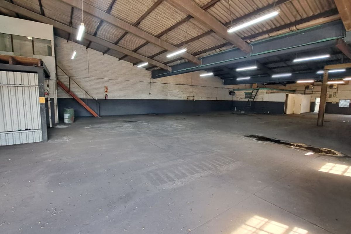 Spacious industrial warehouse unit featuring high ceilings with exposed steel trusses, concrete flooring, and a metal staircase leading to an upper level.