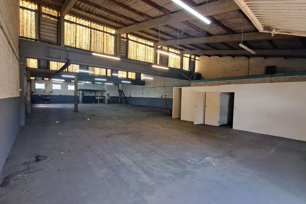 Spacious industrial warehouse featuring high ceilings with exposed steel trusses, concrete flooring, and partitioned office areas, suitable for various commercial or storage uses.