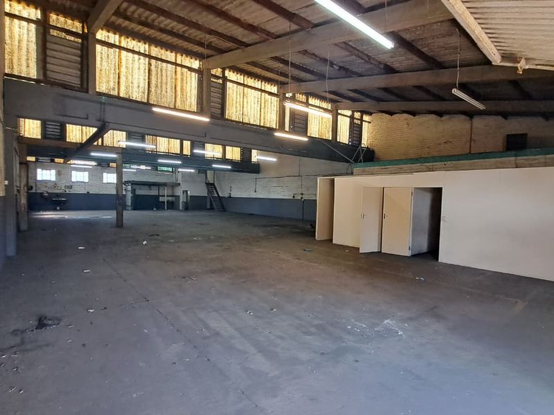 Spacious industrial warehouse featuring high ceilings with exposed steel trusses, concrete flooring, and partitioned office areas, suitable for various commercial or storage uses.