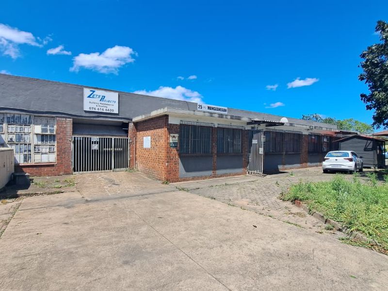 Front exterior view of an industrial property featuring a brick facade, security bars, and a concrete driveway with access to a roller door.