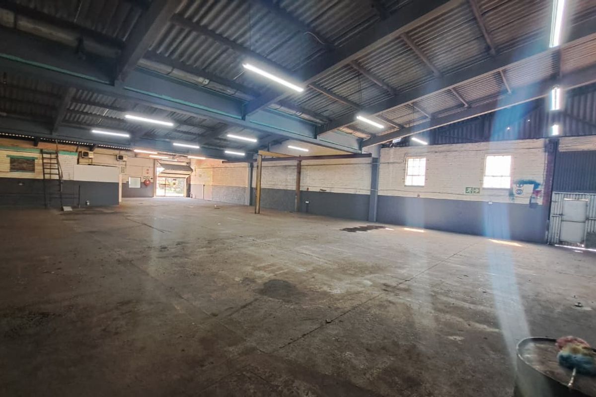 Spacious industrial warehouse featuring high exposed steel trusses, concrete flooring, and ample natural light through side windows, suitable for various commercial or storage uses.