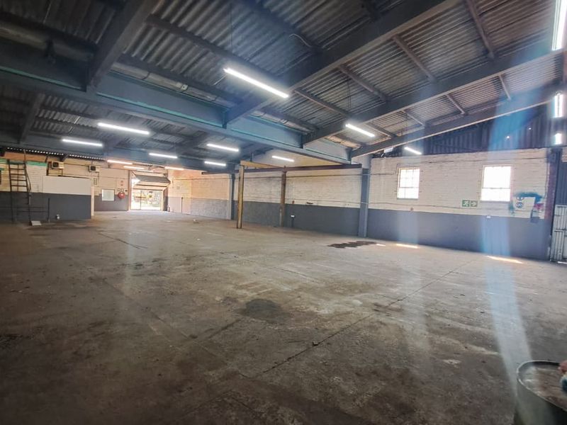 Spacious industrial warehouse featuring high exposed steel trusses, concrete flooring, and ample natural light through side windows, suitable for various commercial or storage uses.