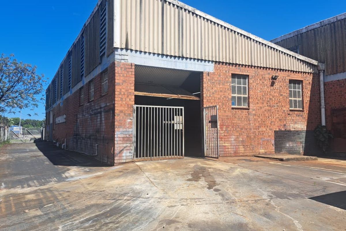 Industrial warehouse exterior featuring brick construction, corrugated metal cladding, and a secure gated entrance with a concrete hardstand area.