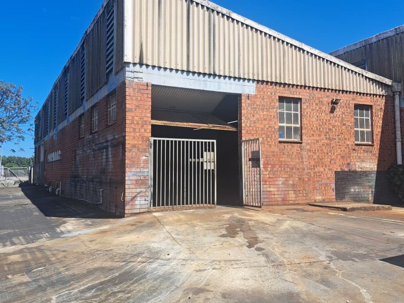 Industrial warehouse exterior featuring brick construction, corrugated metal cladding, and a secure gated entrance with a concrete hardstand area.