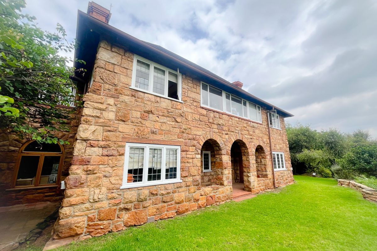 A view of the rear stone facade featuring arched entryways, multi-pane windows, and a well-maintained lawn area.