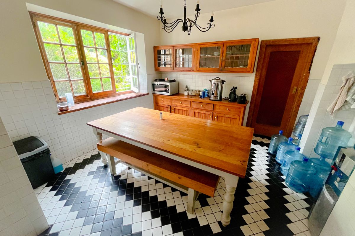 A functional office kitchen area featuring wooden cabinetry, a central wooden table, and classic black and white checkered floor tiles.