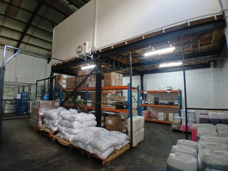 Industrial warehouse utility space featuring a mezzanine level, steel structural framing, wire mesh security partitioning, and concrete flooring.