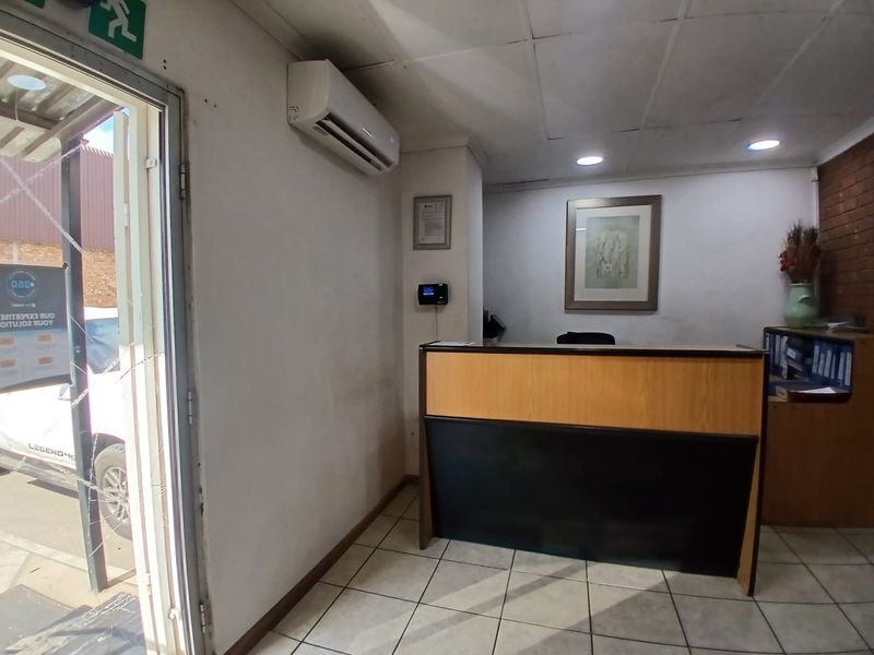 A functional industrial reception area featuring a built-in service counter, tiled flooring, and wall-mounted air conditioning unit.