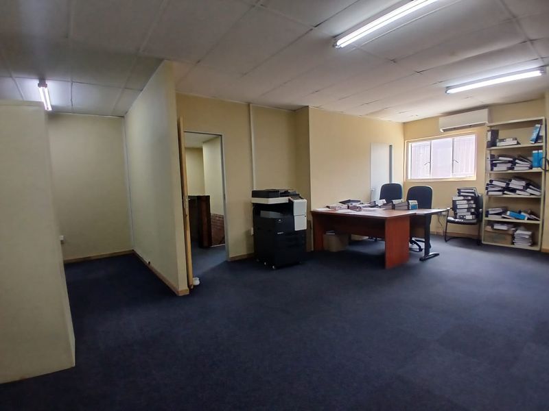 A functional office space featuring carpeted flooring, partition walls, fluorescent lighting, and a wall-mounted air conditioning unit.