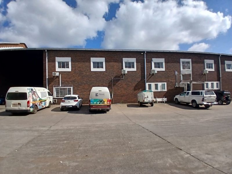 Rear exterior view of an industrial building featuring a brick facade, security-barred windows, and a concrete yard area.