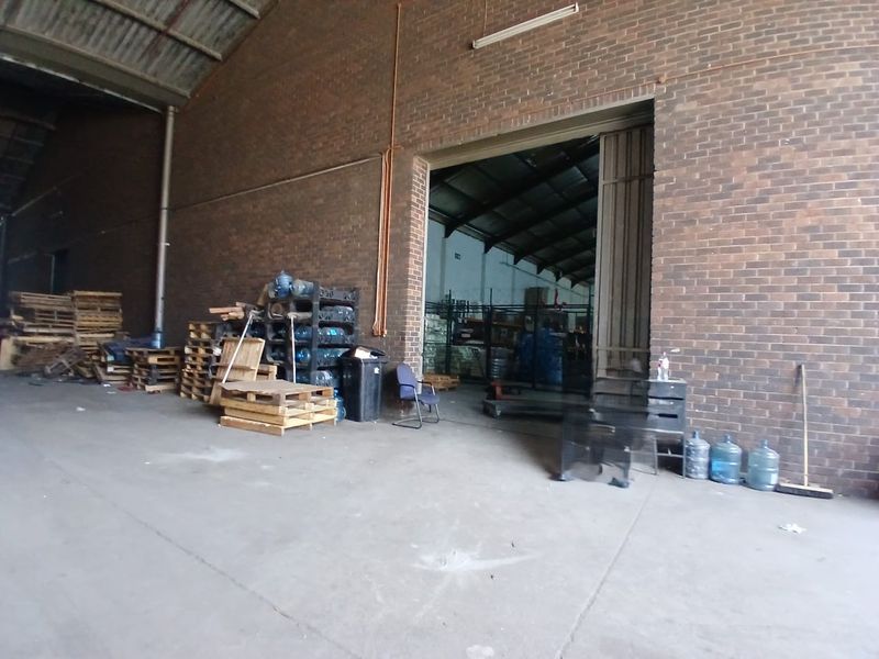 Spacious industrial warehouse utility area featuring exposed brick walls, concrete flooring, and high-clearance roof trusses with a large sliding access door.