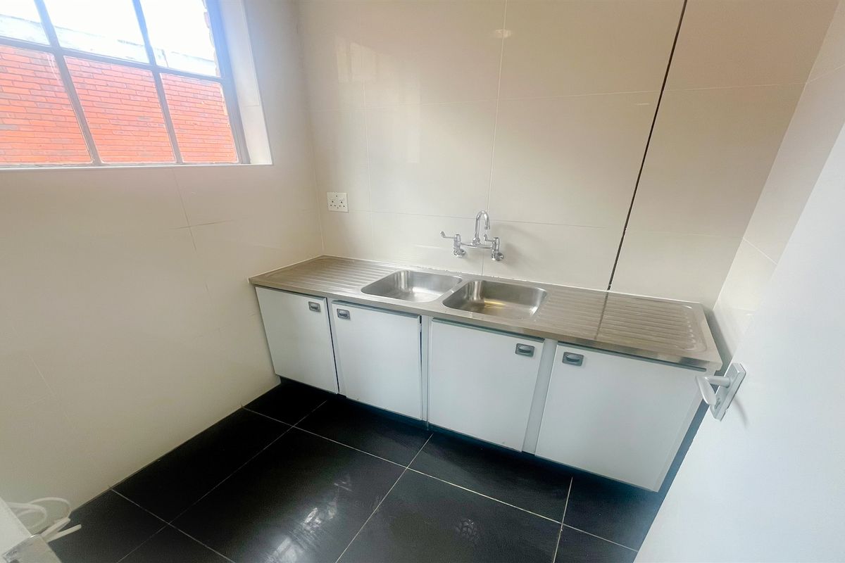 A functional office kitchenette featuring a stainless steel double sink, white cabinetry, and tiled flooring.