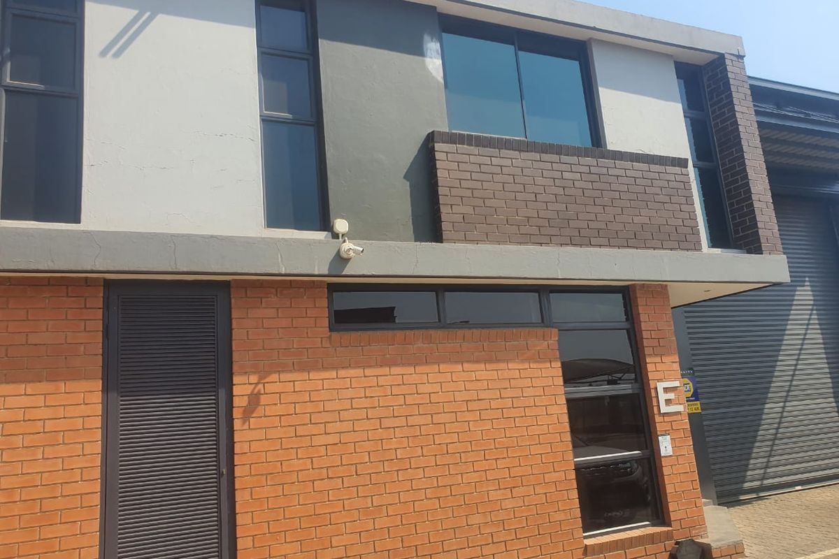 Modern industrial facade featuring a combination of face brick and rendered finishes, large glass windows, and a secure roller shutter door entrance.