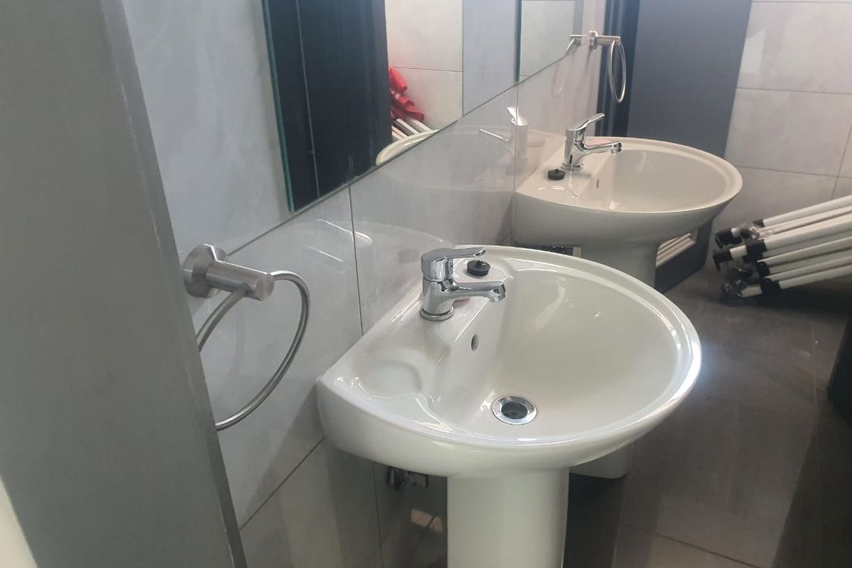 A clean, functional bathroom featuring dual pedestal sinks with chrome faucets and wall-mounted towel rings.