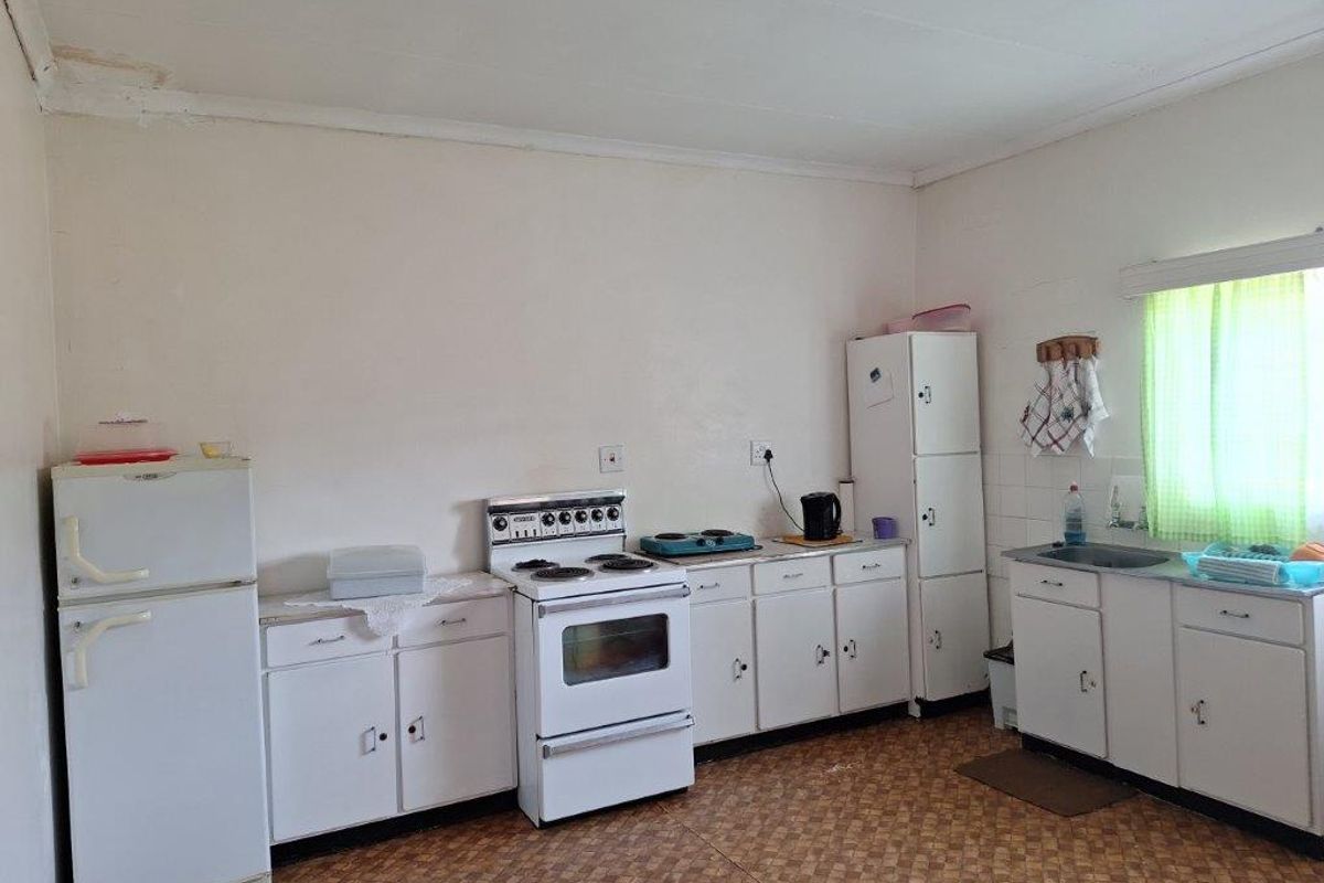 A dated kitchen featuring white cabinetry, a freestanding stove, and a single basin sink with vinyl flooring.