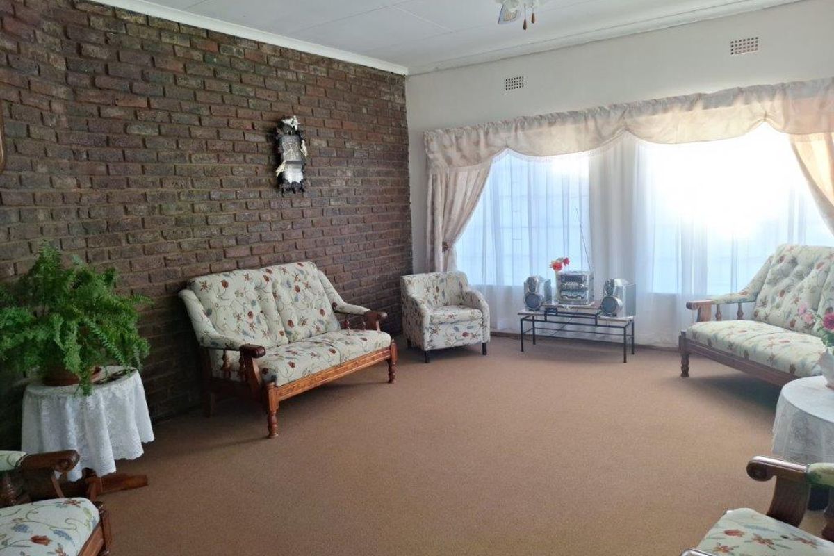 A spacious living room featuring a prominent exposed brick feature wall, carpeted flooring, and large windows allowing for ample natural light.