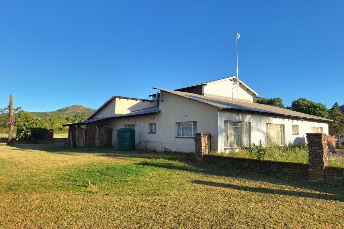 Exterior view of a farm property featuring a single-story dwelling with a metal roof, brick boundary wall, and surrounding rural landscape.