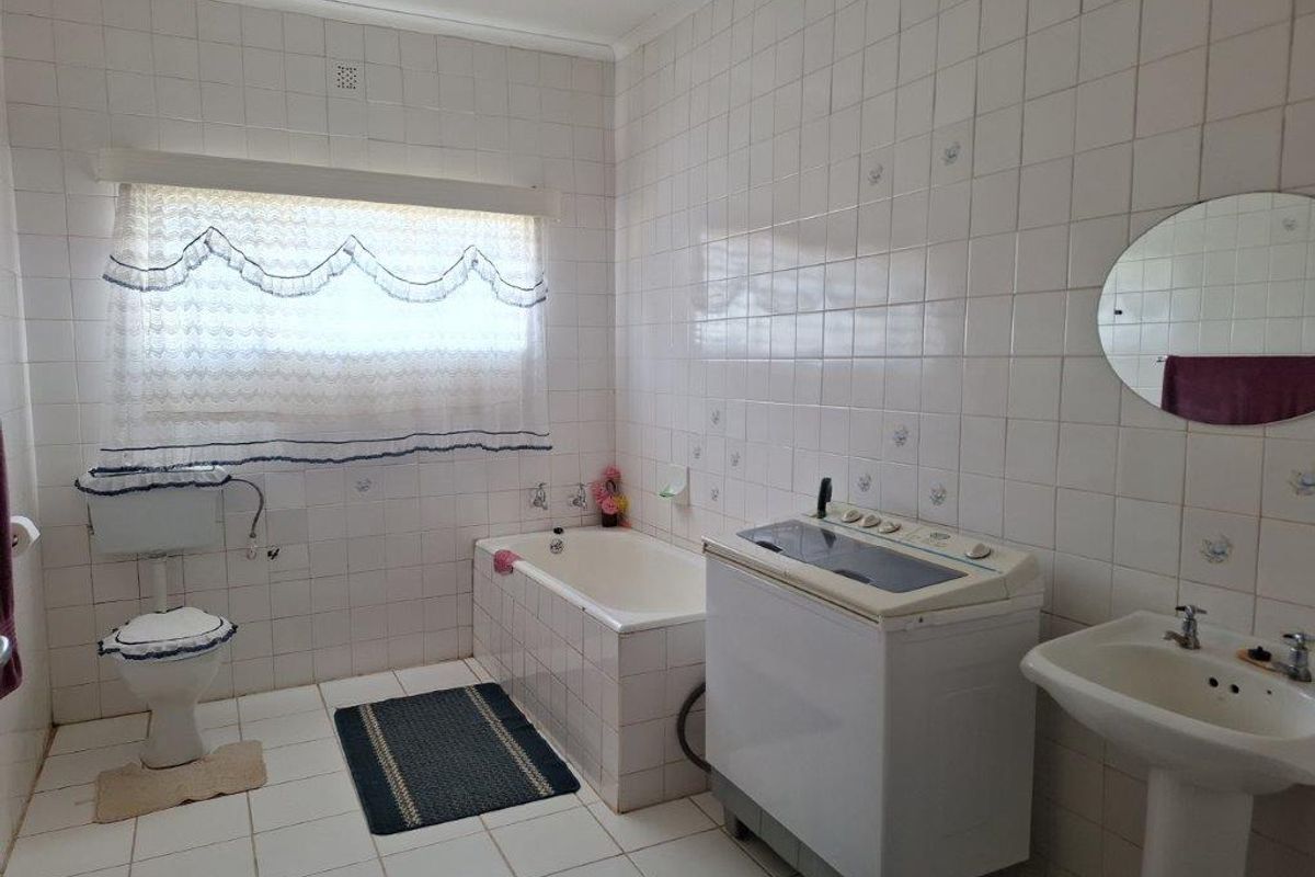 A functional bathroom featuring a pedestal basin, bathtub, and toilet, with full-height wall tiling and a window for natural light.