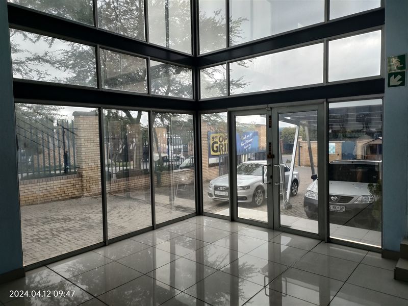 Modern industrial entrance foyer featuring expansive floor-to-ceiling glass panels, double glass doors, and polished porcelain tile flooring.
