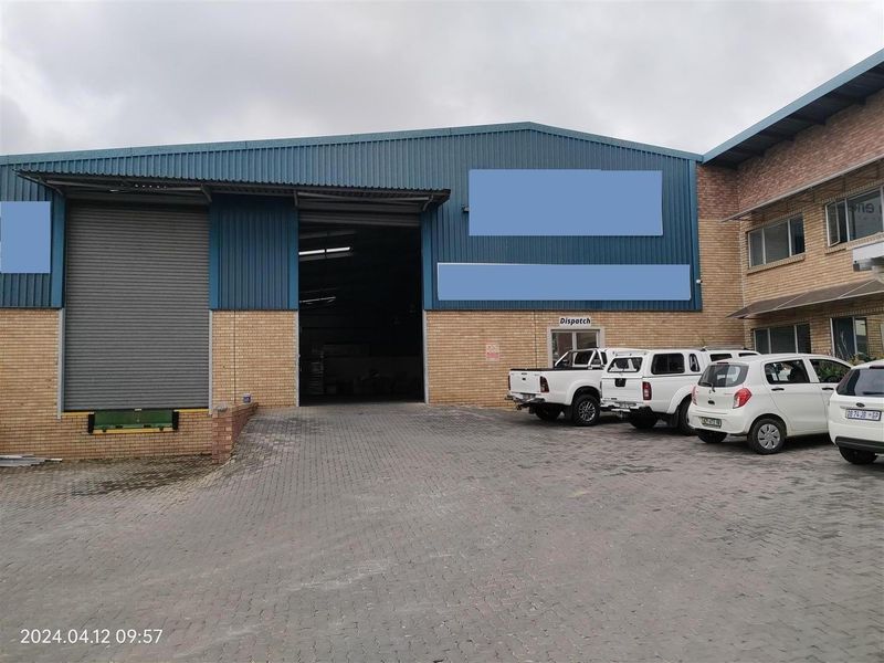 Industrial warehouse exterior featuring a roller shutter door, loading dock, and paved driveway access.