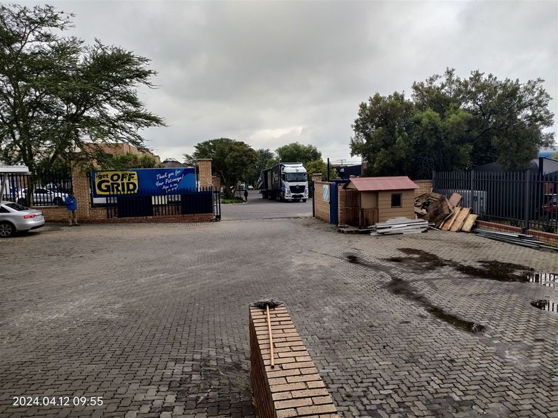 Industrial property entrance featuring a paved driveway, brick boundary walls, and secure metal fencing access point.