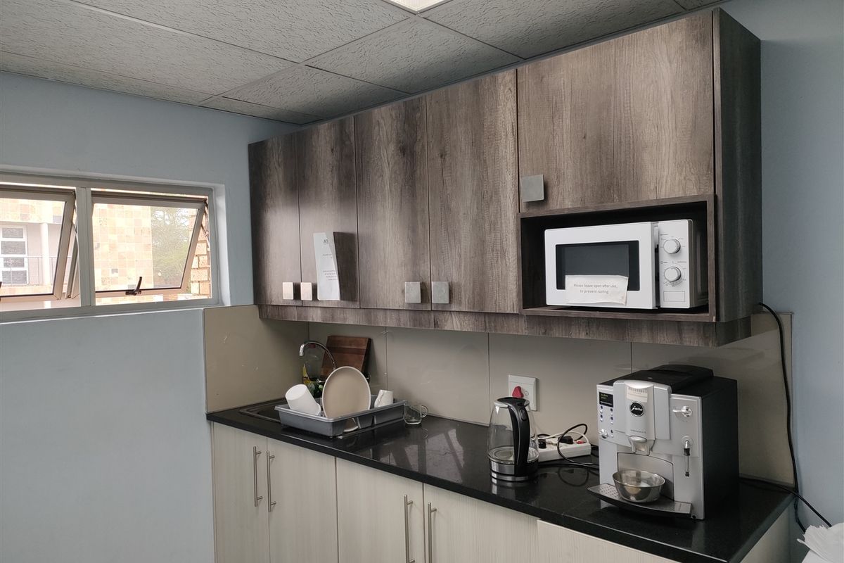 A functional kitchenette featuring modern wood-grain cabinetry, dark laminate countertops, a stainless steel sink, and a built-in microwave.