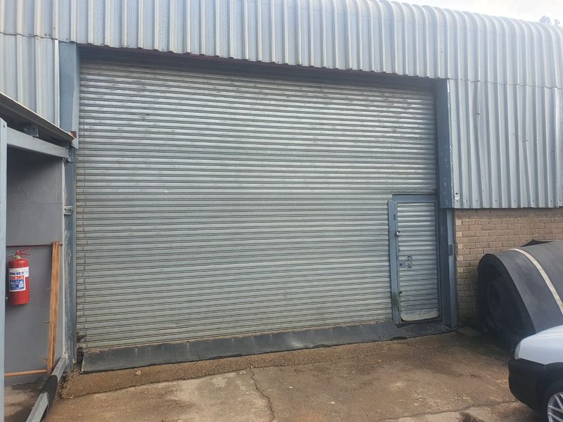 Industrial warehouse exterior featuring a large roller shutter door, integrated pedestrian access, and durable steel cladding construction.