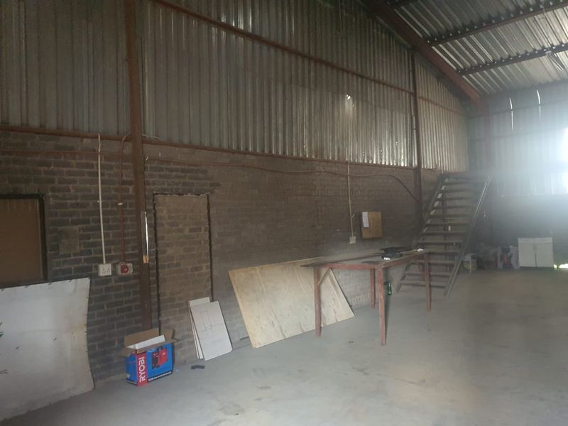 Spacious industrial utility area featuring exposed brick walls, corrugated metal cladding, and a metal staircase, suitable for workshop or storage use.