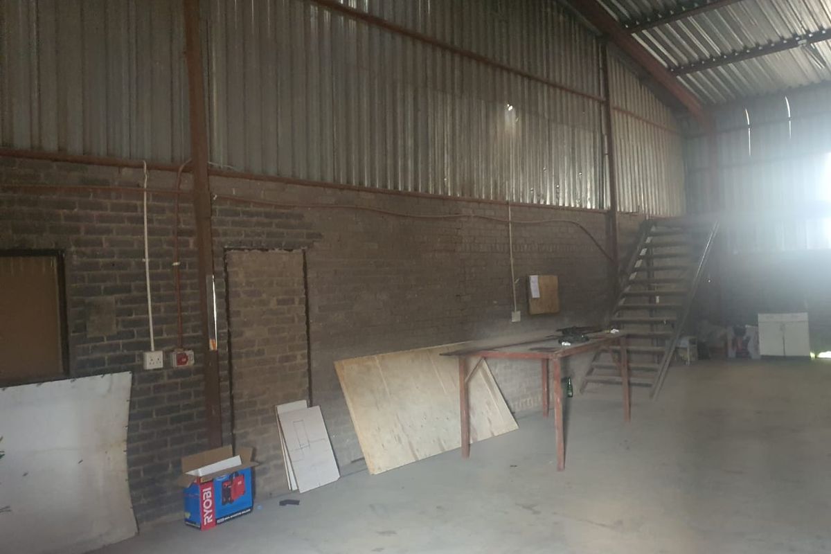 Spacious industrial utility area featuring exposed brick walls, corrugated metal cladding, and a metal staircase, suitable for workshop or storage use.