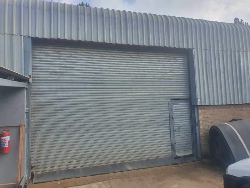 Industrial warehouse exterior featuring a large roller shutter door, integrated personnel access door, and corrugated metal cladding.