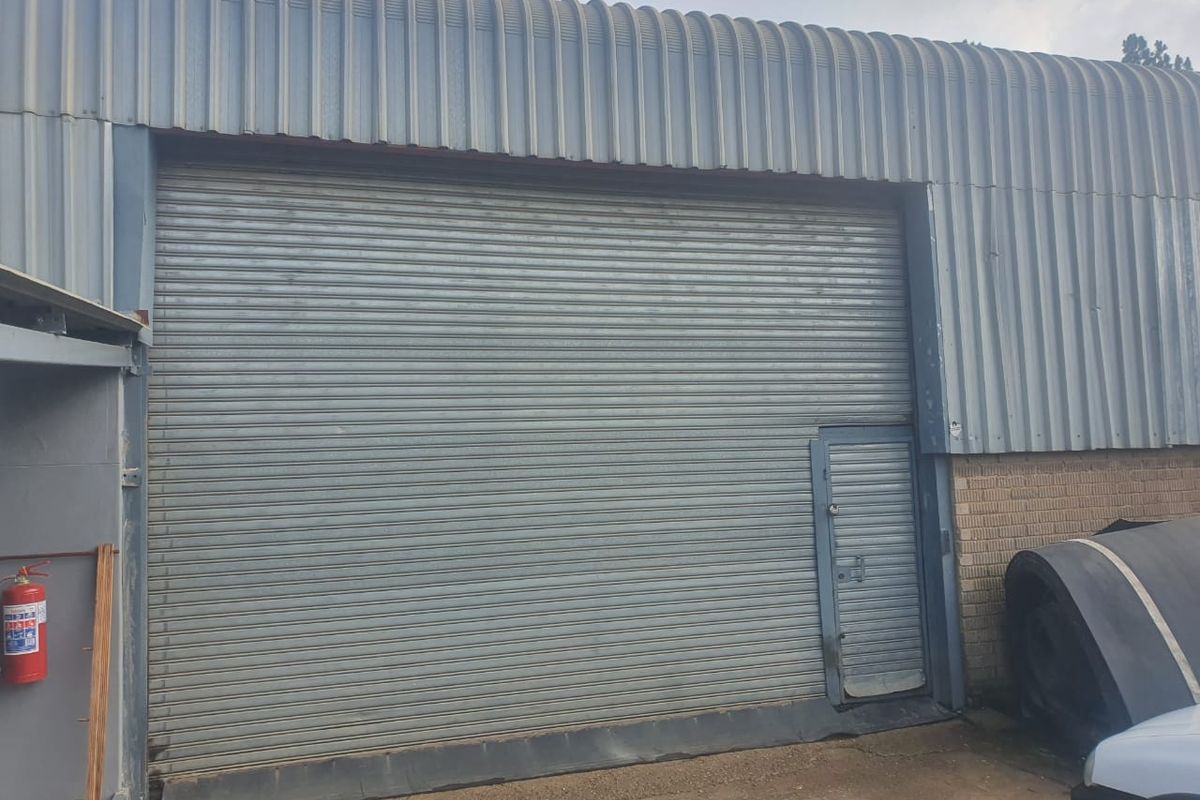 Industrial warehouse exterior featuring a large roller shutter door, integrated personnel access door, and corrugated metal cladding.
