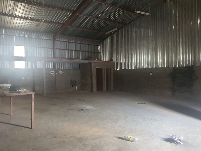 Spacious industrial utility area featuring exposed brick walls, corrugated metal roofing, concrete flooring, and an integrated partitioned office space.
