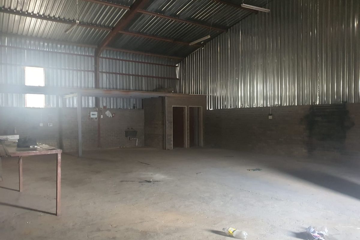 Spacious industrial utility area featuring exposed brick walls, corrugated metal roofing, concrete flooring, and an integrated partitioned office space.