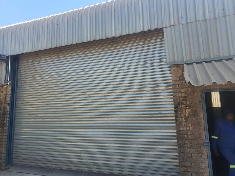 Industrial property exterior featuring a large metal roller shutter door, corrugated metal cladding, and face brick masonry construction.