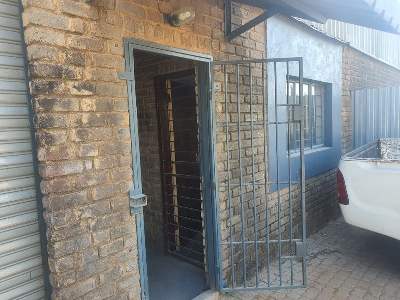 Industrial property entrance featuring a security gate, exposed brick facade, and a roller shutter door for secure access.