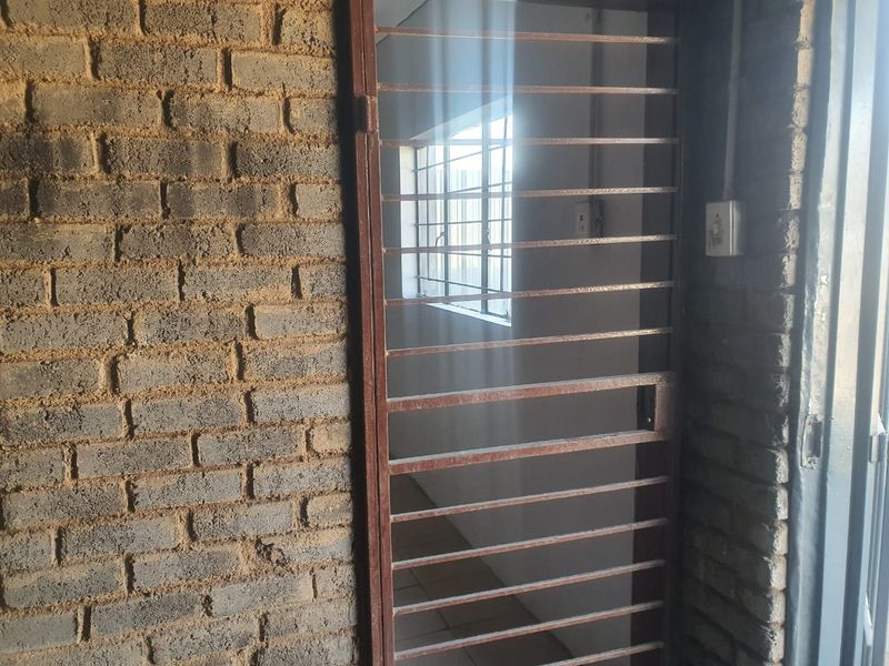A functional hallway area featuring exposed brick walls, tiled flooring, and a secure metal gate, providing a utilitarian industrial aesthetic.