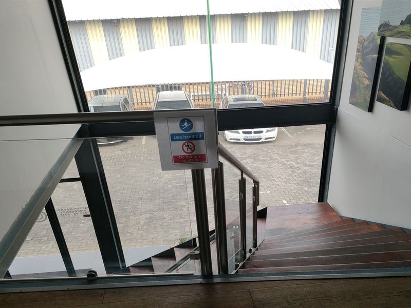 A modern staircase featuring a glass balustrade and stainless steel handrail, overlooking an exterior parking area through a large window.