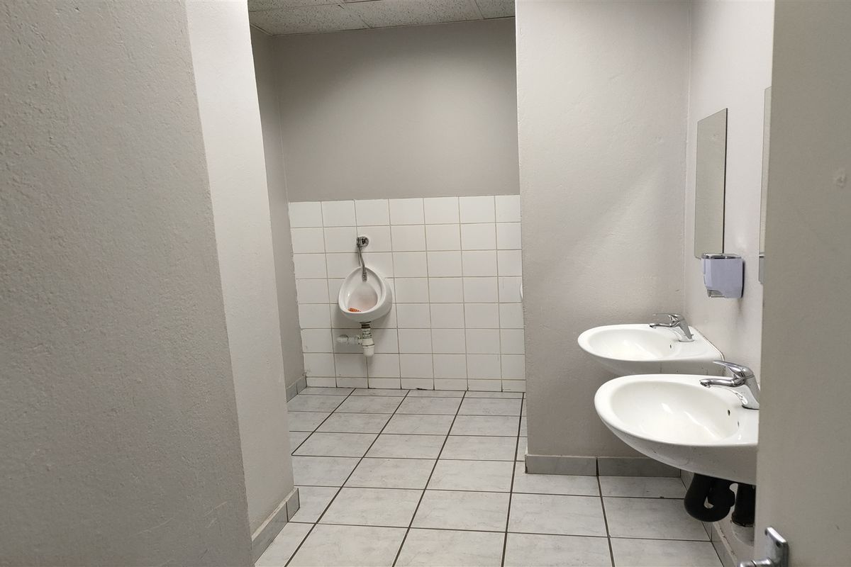 Functional industrial-style restroom featuring wall-mounted washbasins, a urinal, tiled flooring, and tiled splashbacks, requiring some maintenance and cosmetic updates.