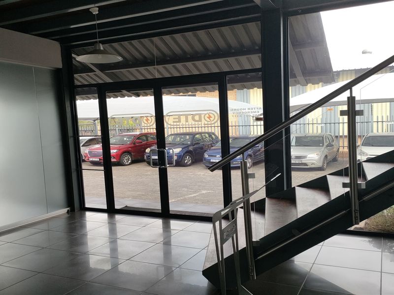 Modern industrial entrance area featuring tiled flooring, a contemporary steel staircase with stainless steel balustrades, and large glass doors leading to the exterior.