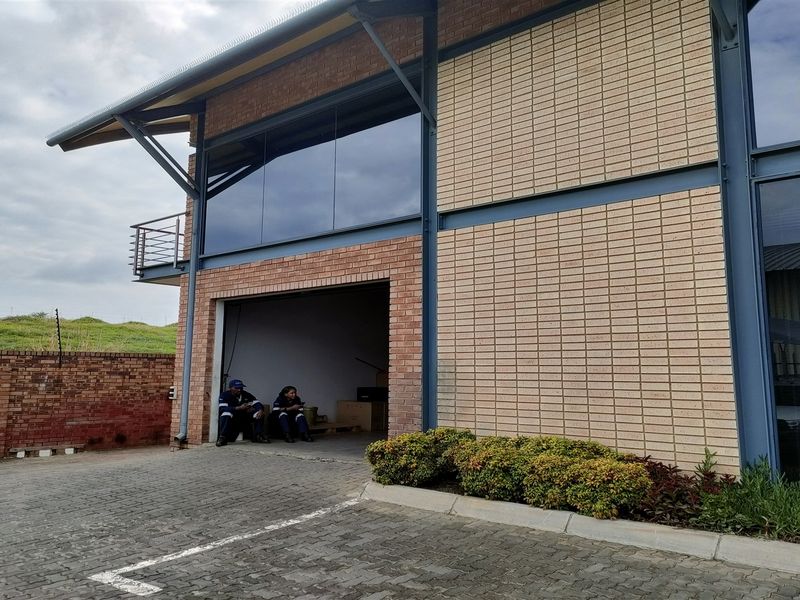 Front view of a modern industrial building featuring brick masonry, steel structural elements, large glass windows, and a paved driveway area.