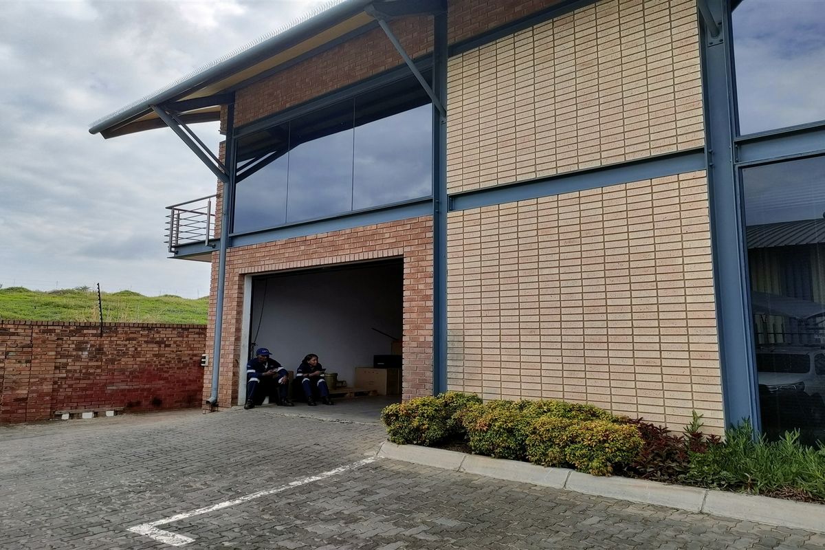 Front view of a modern industrial building featuring brick masonry, steel structural elements, large glass windows, and a paved driveway area.