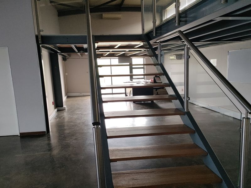 Modern industrial office space featuring a mezzanine level, polished concrete floors, and a contemporary steel staircase with glass balustrades.