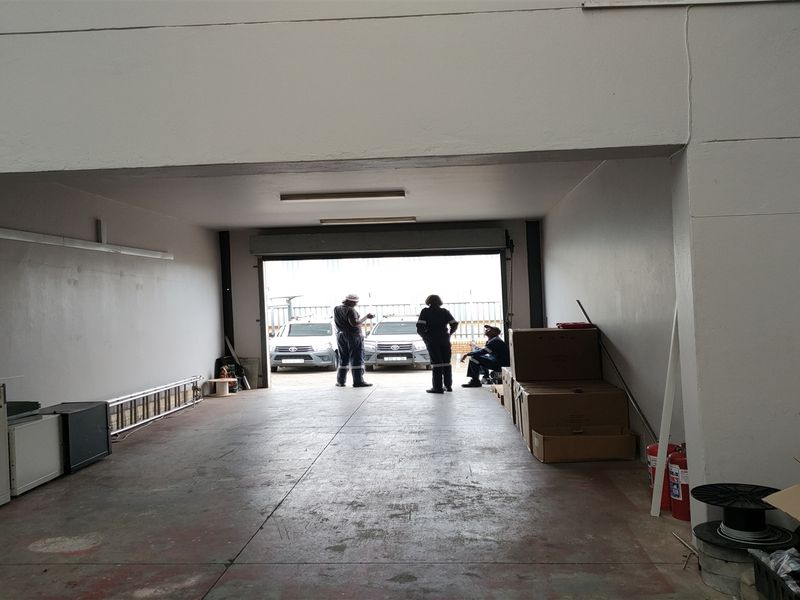 Spacious industrial garage area featuring concrete flooring, roller shutter door access, and functional overhead lighting, suitable for storage or workshop use.