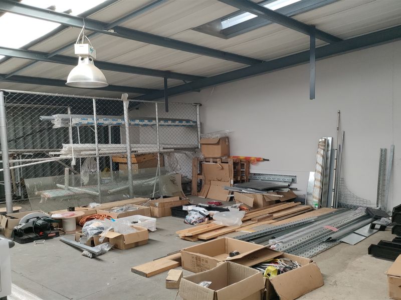 Industrial utility space featuring exposed steel roof framing, skylights, concrete flooring, and a secure chain-link partitioned storage area.