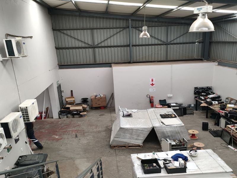 Spacious industrial utility area featuring high ceilings with exposed steel trusses, concrete flooring, wall-mounted air conditioning units, and functional industrial lighting.