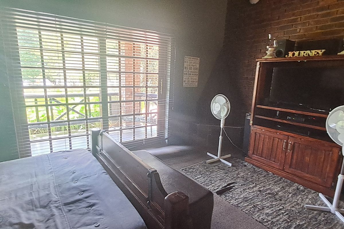 A bedroom featuring an exposed brick wall, a built-in fireplace, and a large sliding glass door with venetian blinds providing natural light.