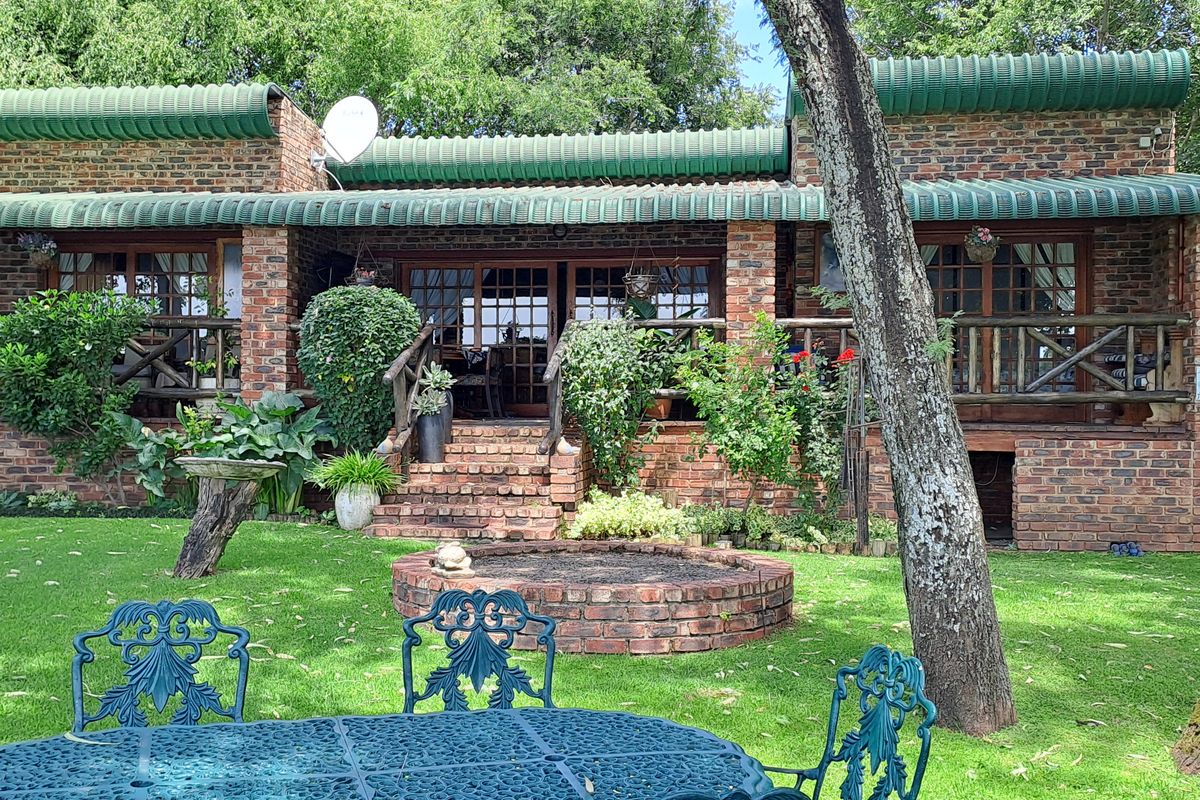Rear view of a face-brick small holding residence featuring a covered patio, timber railings, and a landscaped garden with a built-in brick fire pit.
