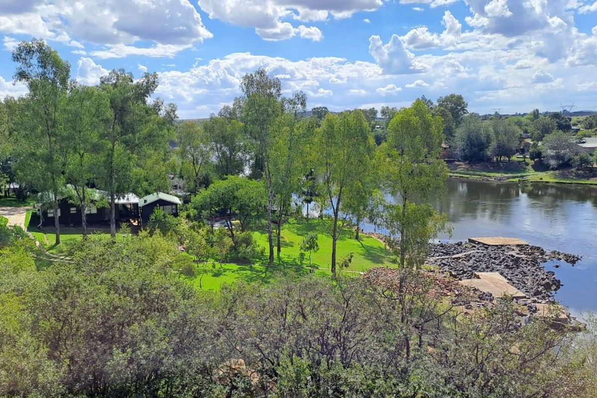 An elevated aerial view of the small holding property, showcasing extensive river frontage, lush green lawns, mature trees, and a stone-reinforced bank.