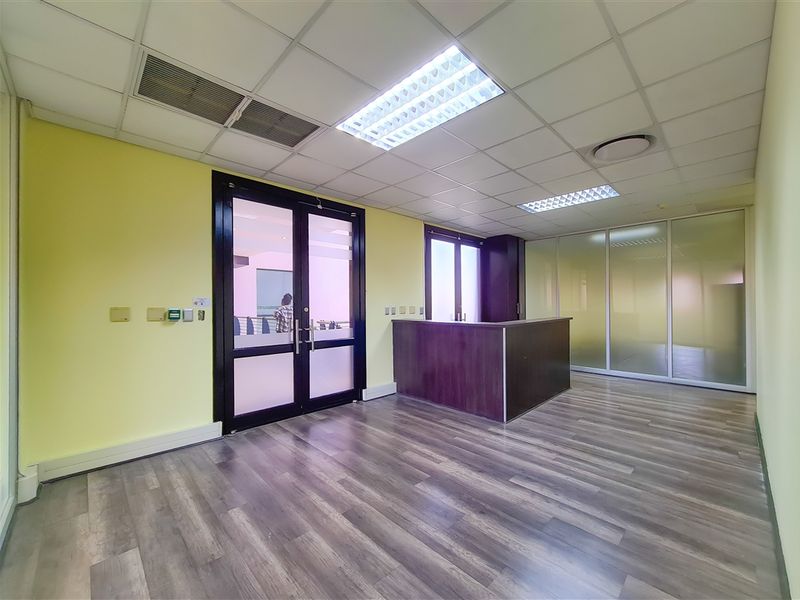 A professional office space featuring laminate flooring, a built-in reception desk, frosted glass partitions, and a suspended ceiling with recessed lighting.